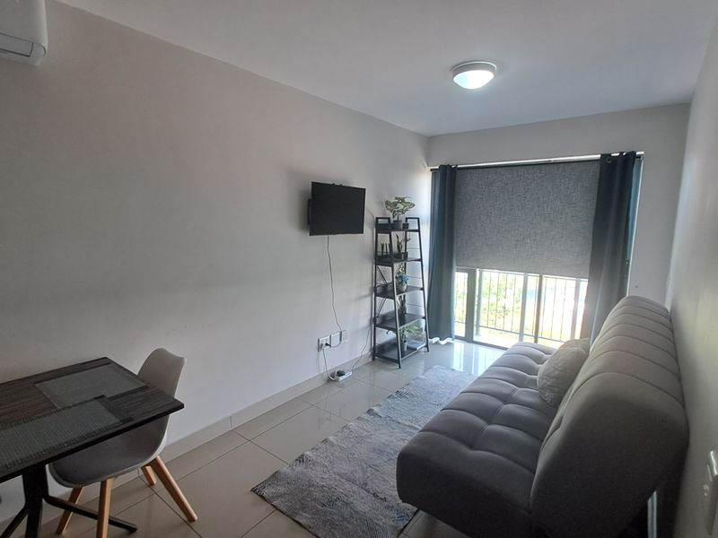 A compact living area featuring tiled flooring, an air conditioning unit, and a sliding glass door with a roller blind and security gate.