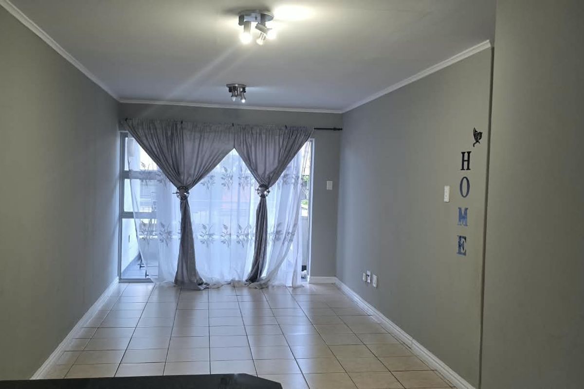 An empty living room featuring tiled flooring and a sliding glass door leading to an outdoor area, providing natural light and access.
