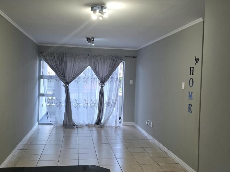 An empty living room featuring tiled flooring and a sliding glass door leading to an outdoor area, providing natural light and access.