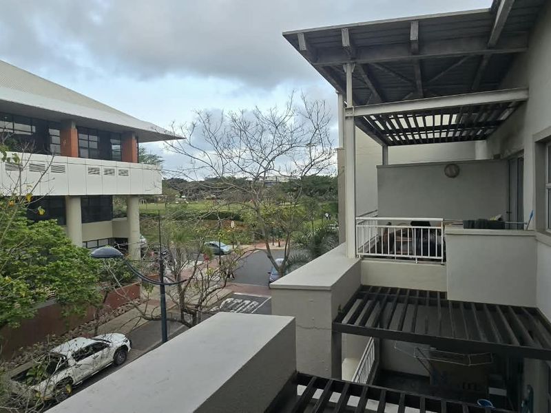 An elevated balcony featuring a metal pergola structure, providing outdoor space with views of the surrounding complex and street.
