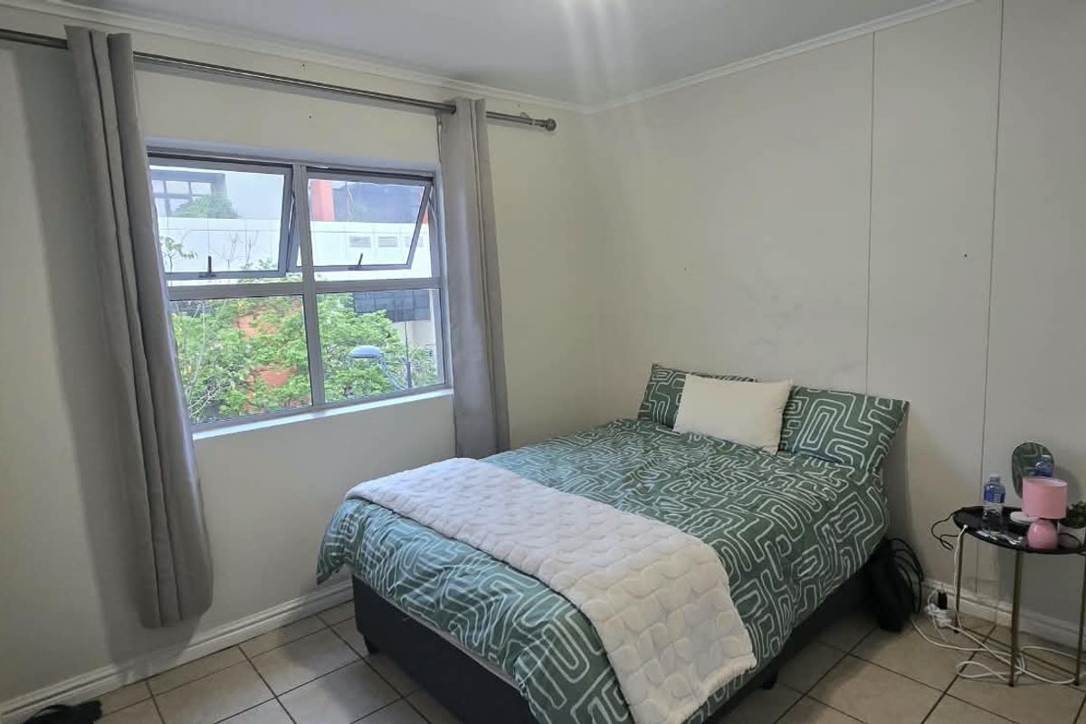 A functional bedroom featuring tiled flooring, a top-hung window with curtain rod, and neutral wall finishes.