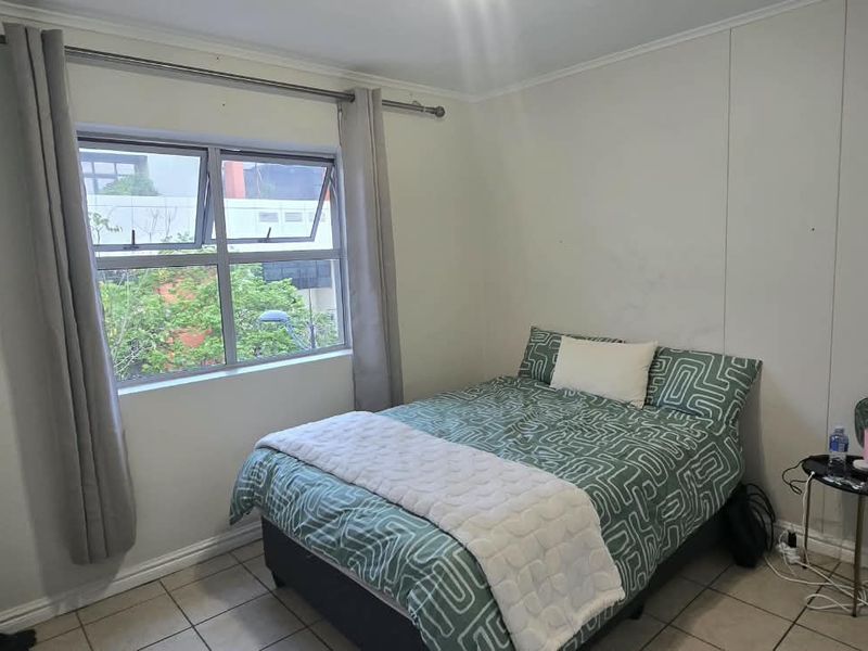 A functional bedroom featuring tiled flooring, a top-hung window with curtain rod, and neutral wall finishes.