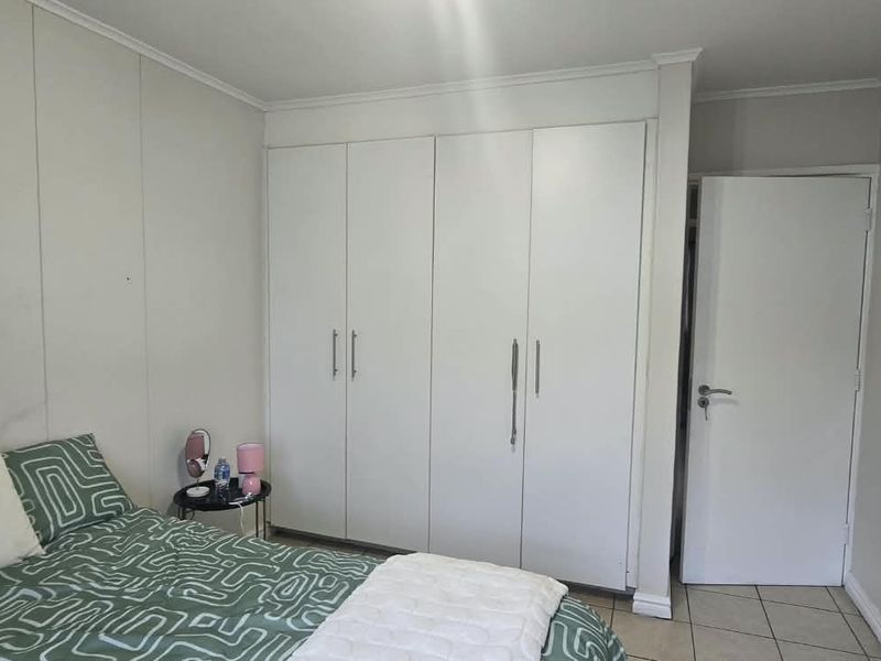 A bedroom featuring built-in cupboards, tiled flooring, and a neutral wall finish, providing a functional and clean living space.