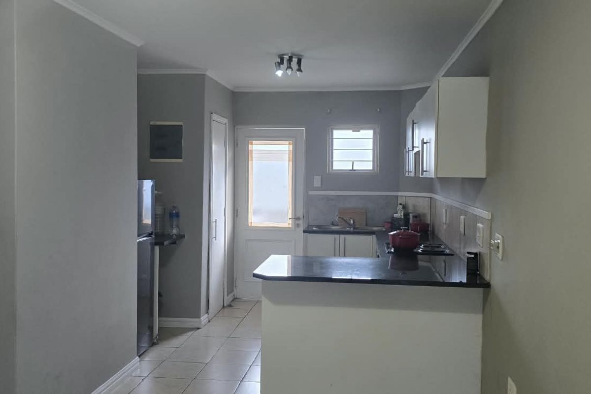 A functional kitchen featuring granite countertops, built-in cabinetry, and tiled flooring, with direct access to an exterior door.