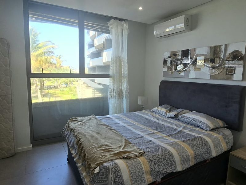 A modern bedroom featuring built-in cupboards, tiled flooring, a split-system air conditioner, and a large window providing natural light.