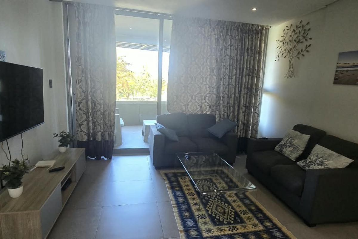 A well-lit living room featuring tiled flooring and large sliding glass doors that provide direct access to an outdoor balcony area.