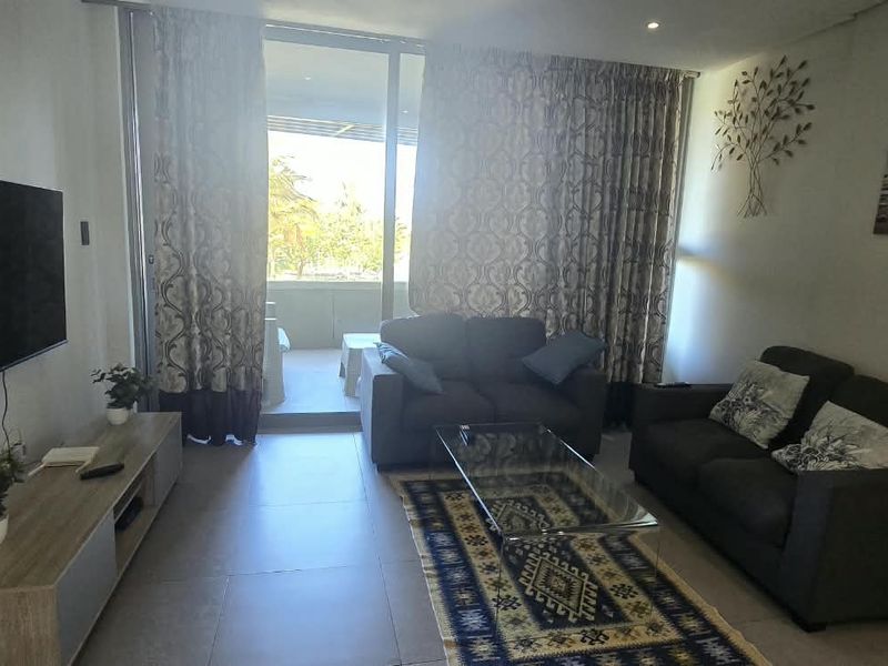 A well-lit living room featuring tiled flooring and large sliding glass doors that provide direct access to an outdoor balcony area.