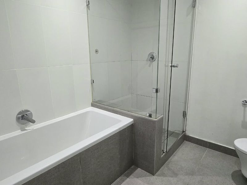 Modern bathroom featuring a white bathtub, separate glass-enclosed shower, and toilet with neutral wall and floor tiling.