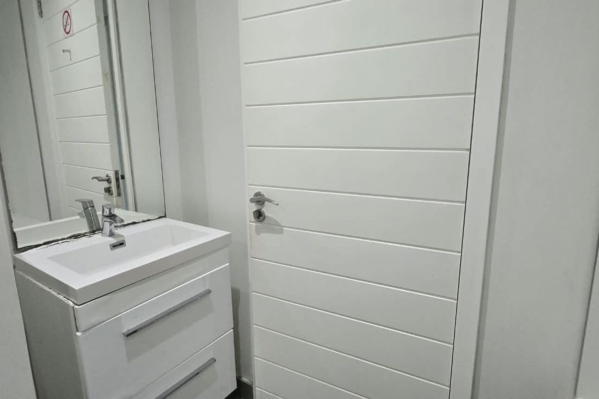 A clean, modern bathroom featuring a white vanity cabinet with a basin, mixer tap, and a wall-mounted mirror.