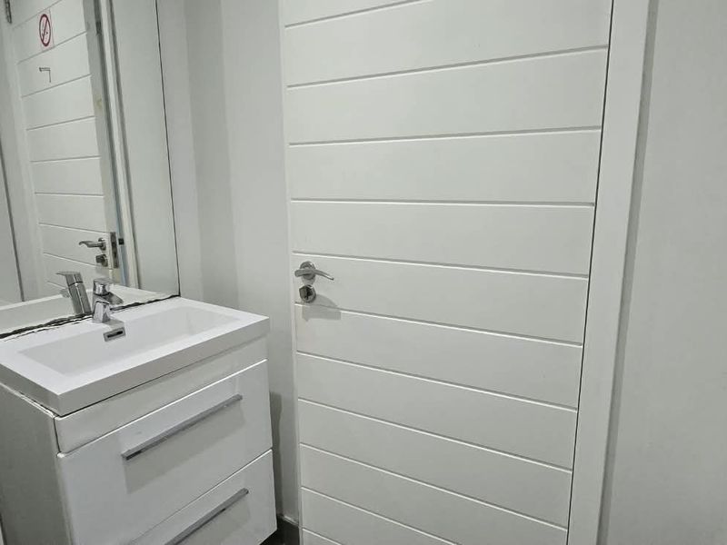 A clean, modern bathroom featuring a white vanity cabinet with a basin, mixer tap, and a wall-mounted mirror.