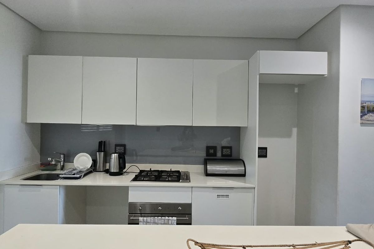 Modern kitchen featuring white cabinetry, stone countertops, a glass splashback, and integrated gas hob with oven.