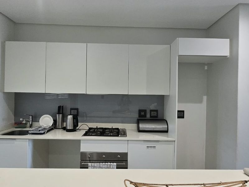 Modern kitchen featuring white cabinetry, stone countertops, a glass splashback, and integrated gas hob with oven.