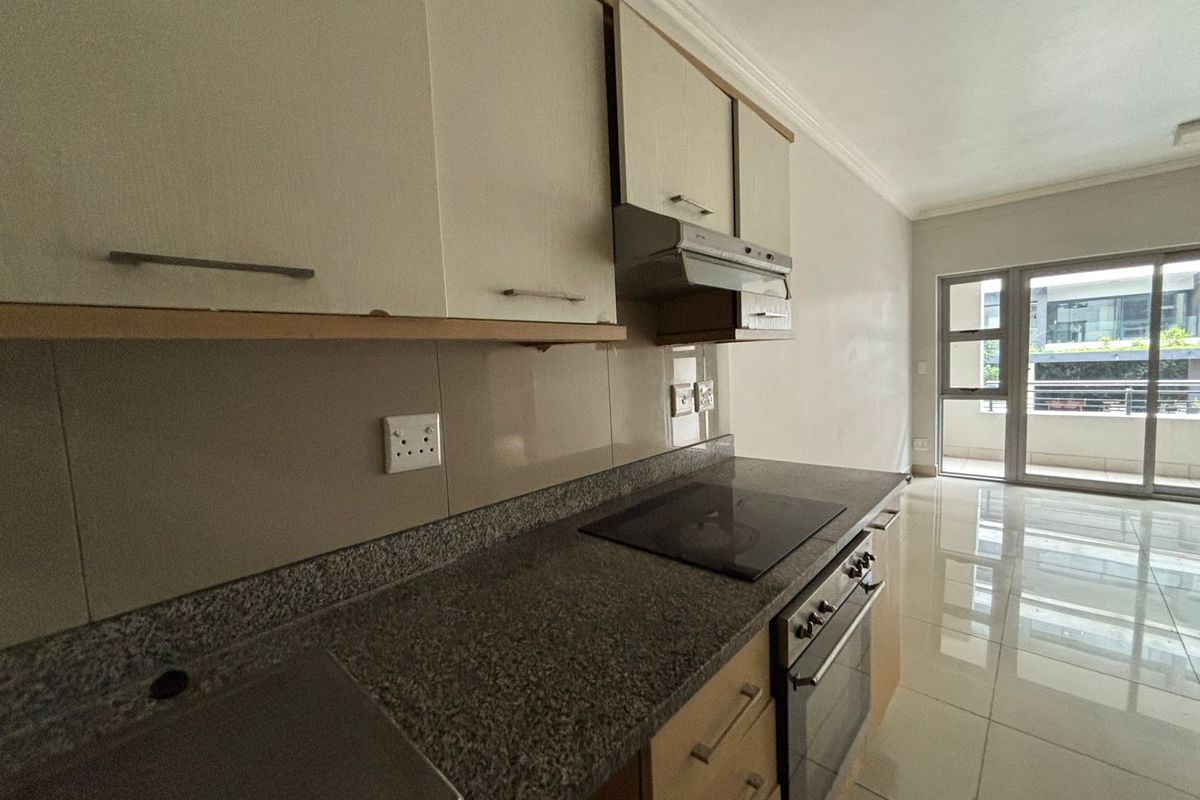 A functional kitchen featuring granite countertops, built-in oven, electric hob, and extractor fan, with tiled flooring and direct access to a balcony.