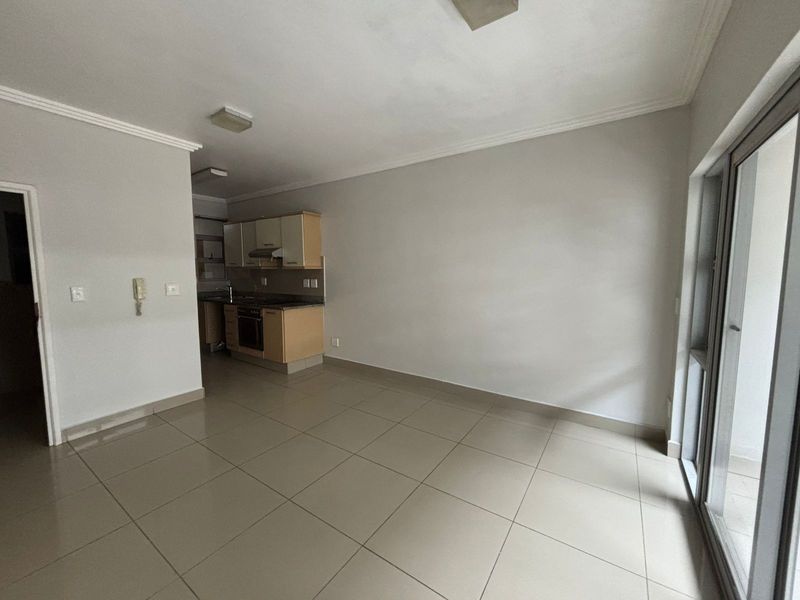 An open-plan living area featuring tiled flooring, a compact kitchen with built-in cabinetry and appliances, and access to an outdoor space via sliding doors.