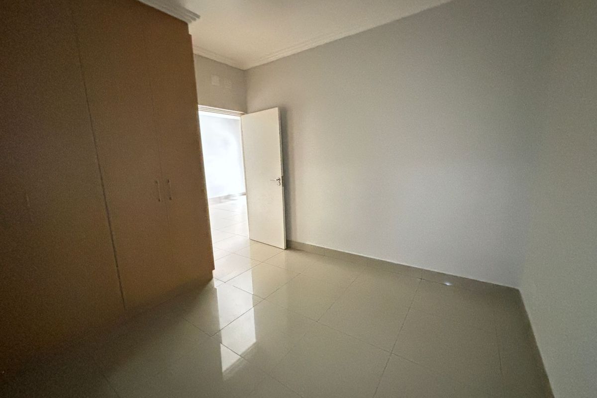 A clean, empty bedroom featuring neutral tiled flooring and ample built-in cupboard storage space.