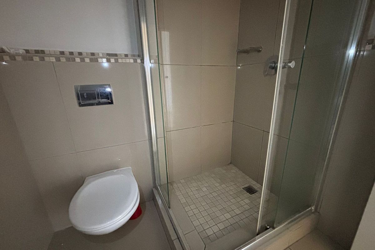 A functional bathroom featuring a wall-mounted toilet and a glass-enclosed shower with tiled finishes.