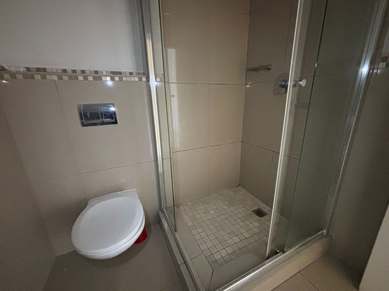 A functional bathroom featuring a wall-mounted toilet and a glass-enclosed shower with tiled finishes.