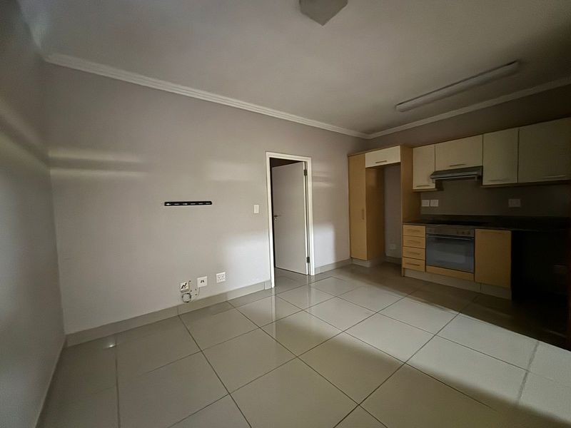 An open-plan living and kitchen area featuring tiled flooring, built-in cabinetry, and integrated kitchen appliances in a neutral, vacant space.