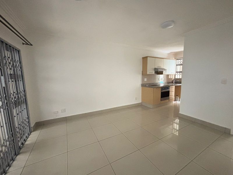 An open-plan living area featuring tiled floors and a compact kitchen with built-in cabinetry, granite countertops, and integrated oven and extractor fan.