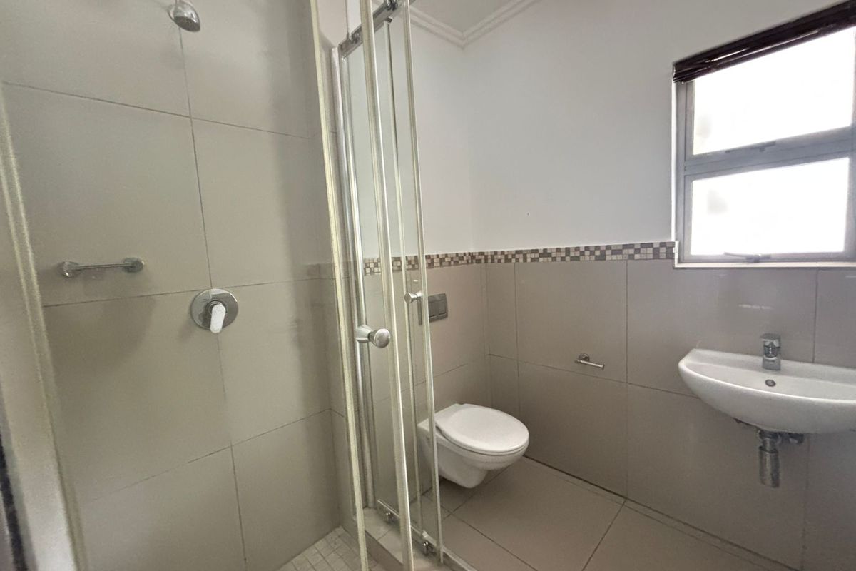 A clean, modern bathroom featuring a glass-enclosed shower, wall-mounted toilet, and a wall-mounted basin with neutral floor-to-ceiling tiling.