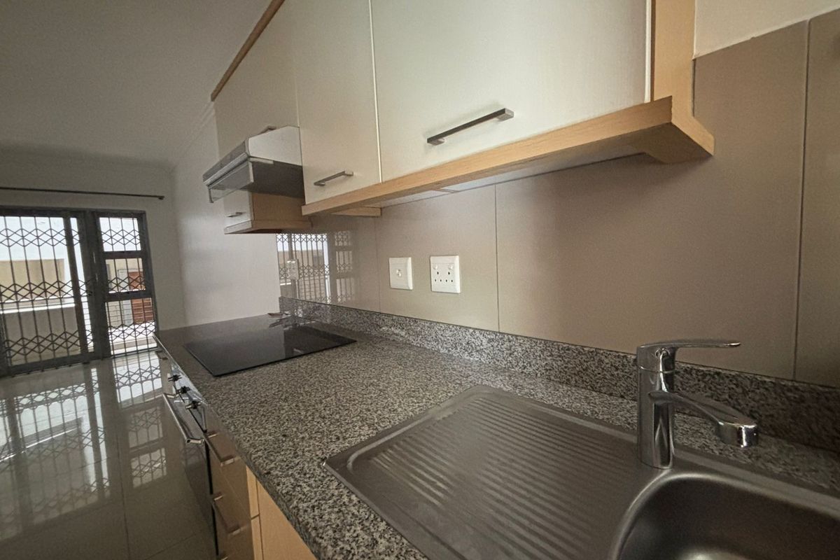 Modern kitchen featuring granite countertops, built-in oven, electric hob, extractor fan, and ample cabinetry, finished with sleek tiled flooring.