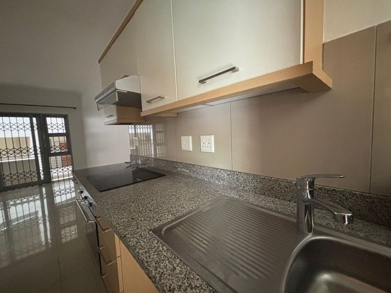 Modern kitchen featuring granite countertops, built-in oven, electric hob, extractor fan, and ample cabinetry, finished with sleek tiled flooring.
