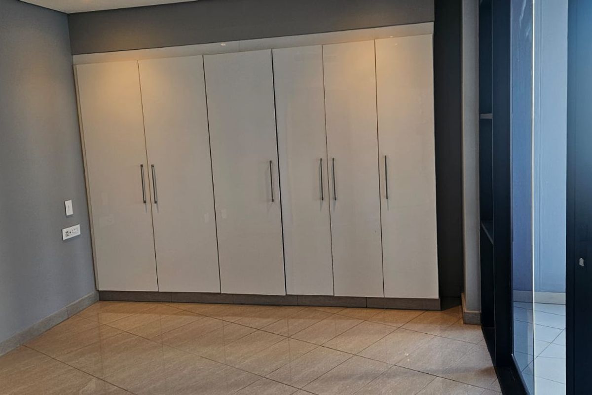 A bright bedroom featuring modern built-in cupboards, polished tile flooring, and a sliding glass door providing access to an outdoor balcony area.