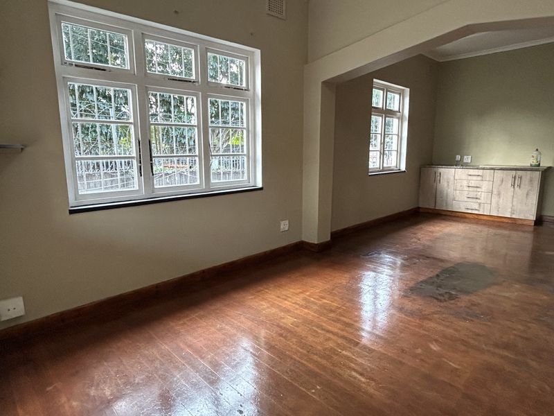 An empty open-plan living area featuring polished wooden floors, built-in cabinetry, and large windows with security bars.