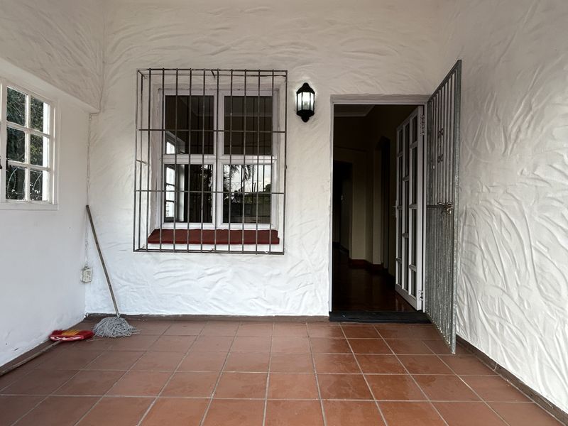 Covered entrance area featuring tiled flooring, textured walls, and security fixtures including a gate and window bars.