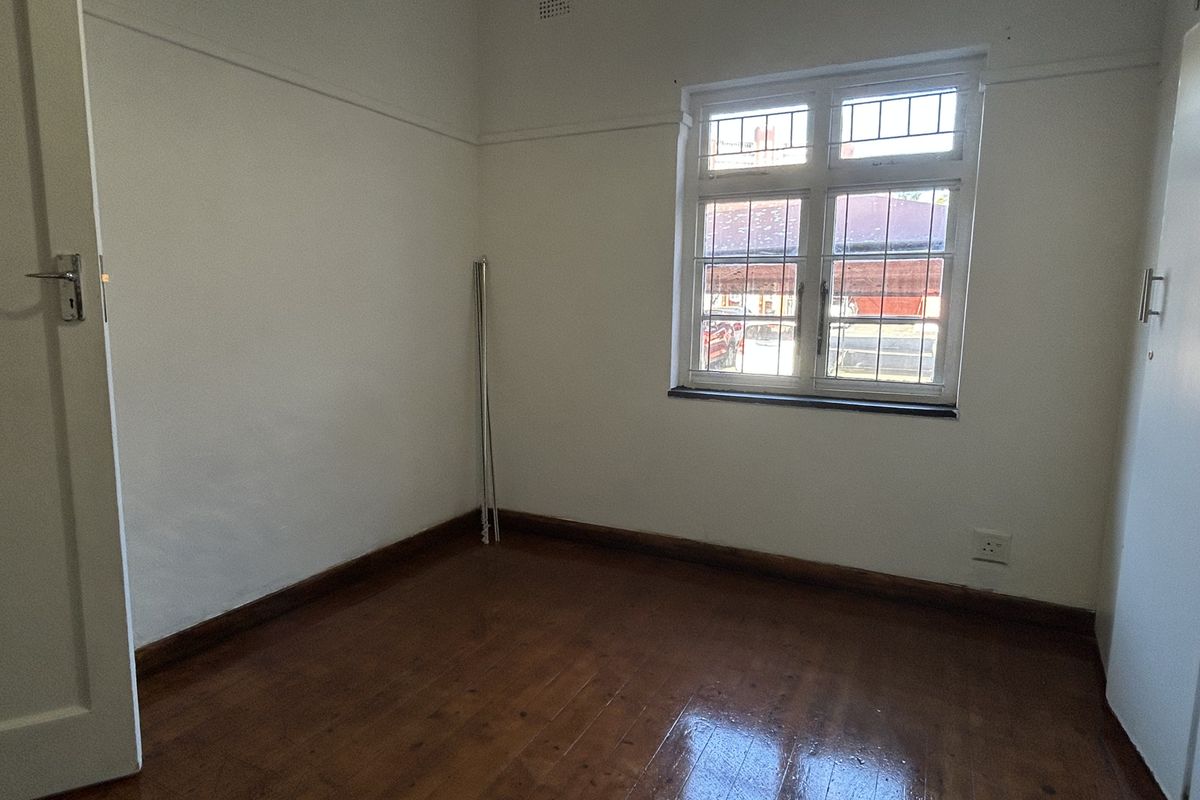 An empty bedroom featuring original timber flooring, a leaded glass window, and a built-in cupboard, offering a blank canvas for personalization.