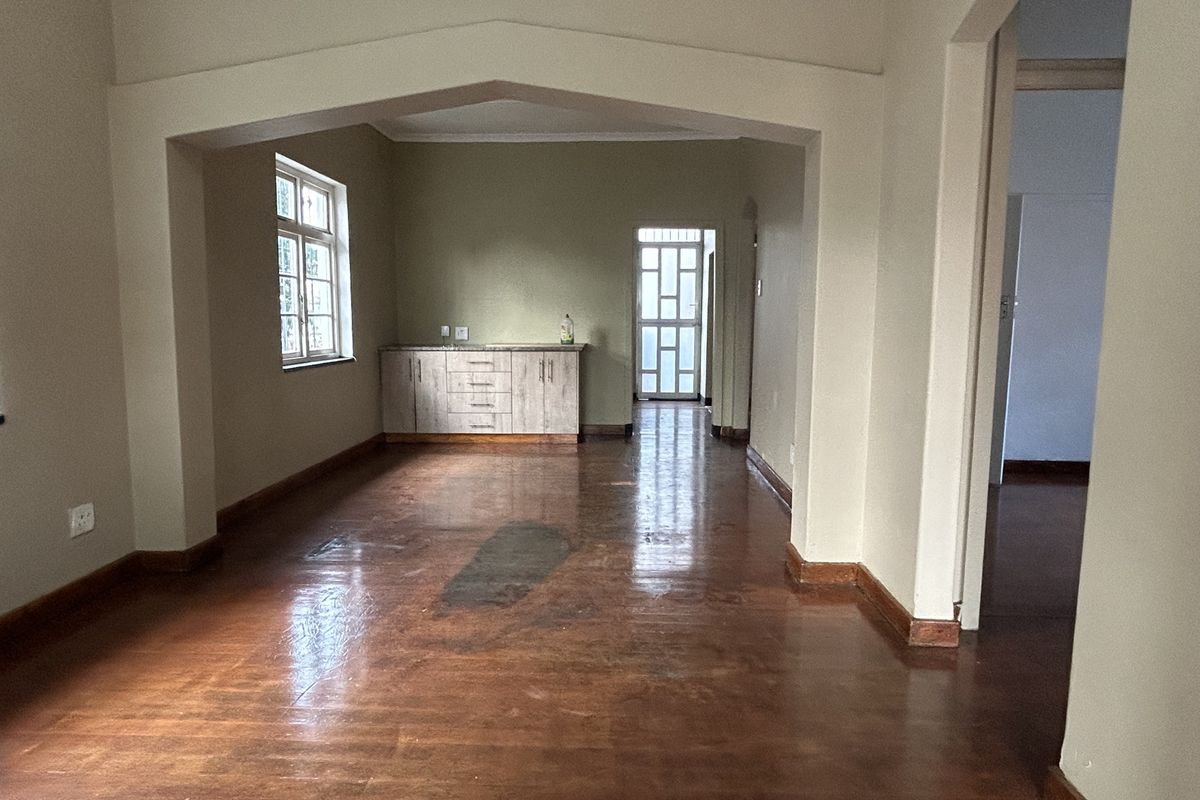 An empty living area featuring polished wooden floors, a decorative archway, and built-in cabinetry, leading to a rear exit with a security gate.