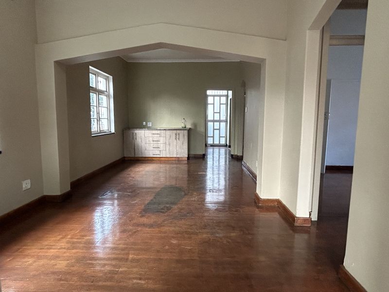 An empty living area featuring polished wooden floors, a decorative archway, and built-in cabinetry, leading to a rear exit with a security gate.