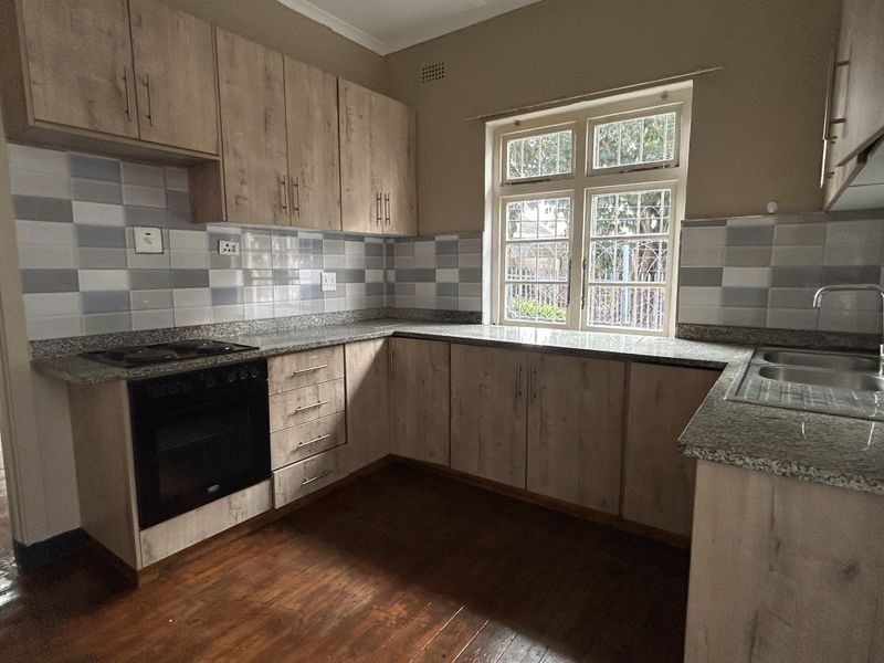 A functional kitchen featuring light wood-look cabinetry, granite countertops, a built-in oven and hob, and a double sink with a tiled backsplash.
