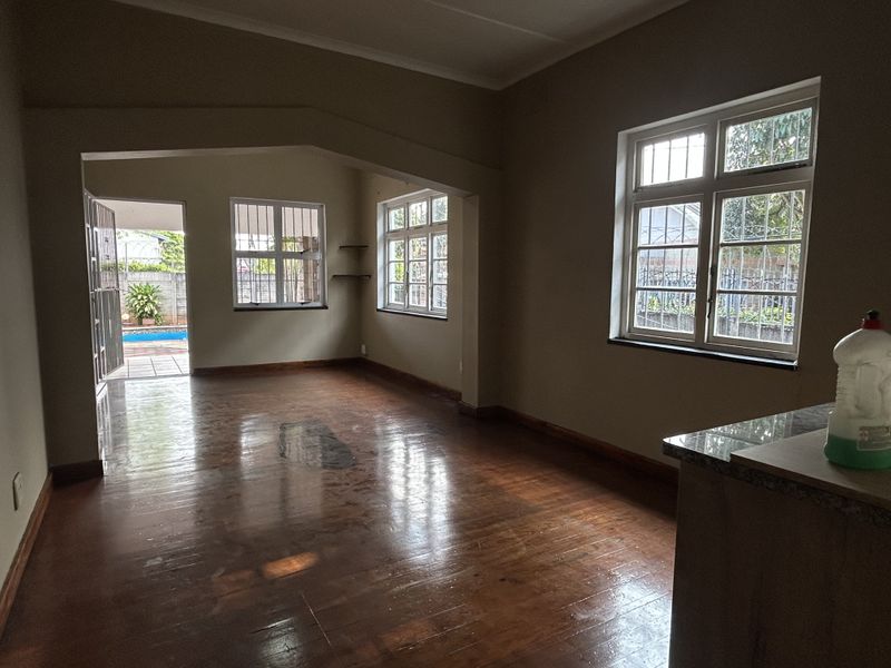 Spacious open-plan living area featuring polished hardwood floors, security-fitted windows, and direct access to an outdoor patio and pool area.