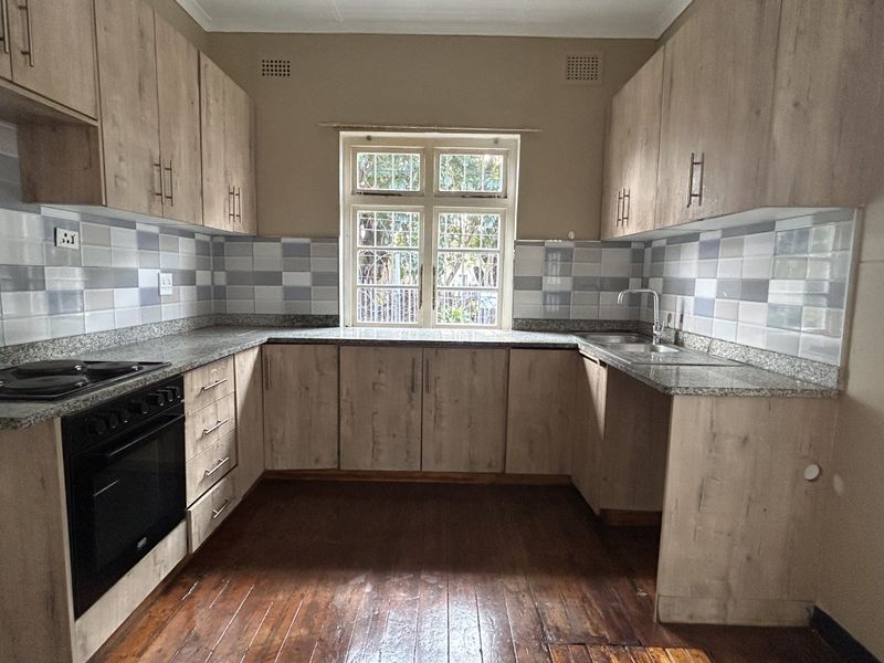 A functional kitchen featuring light wood cabinetry, granite countertops, a tiled backsplash, and a built-in oven with hob, set against warm wooden flooring.