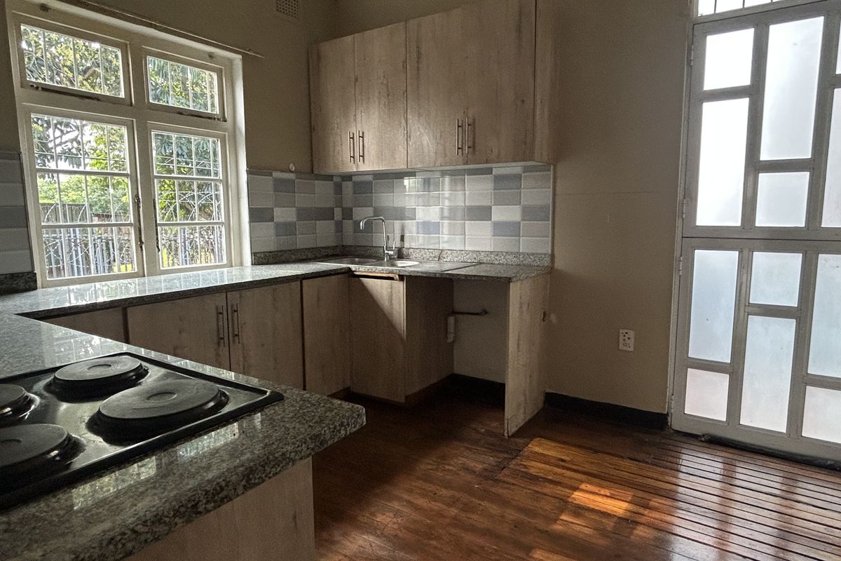 A functional kitchen featuring light wood cabinetry, granite countertops, an electric hob, and direct access to the exterior through a glazed door.