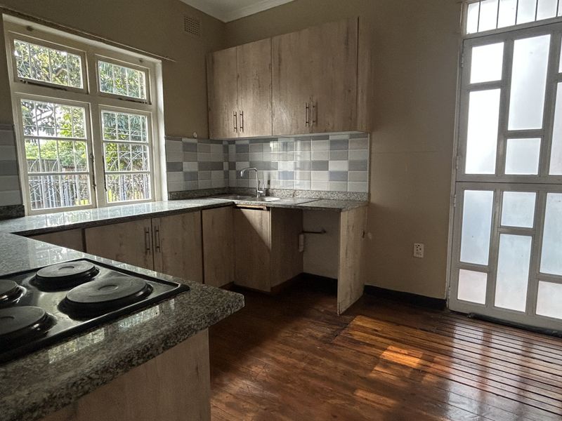 A functional kitchen featuring light wood cabinetry, granite countertops, an electric hob, and direct access to the exterior through a glazed door.