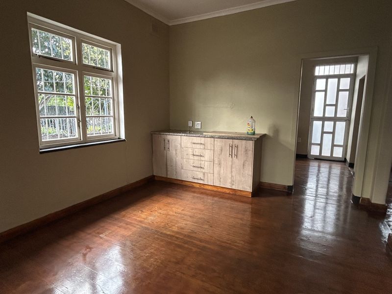 A functional scullery or utility area featuring built-in cabinetry, laminate countertops, and polished wooden flooring with natural light from the window.