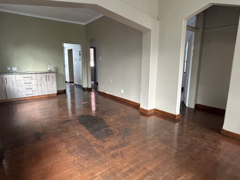 An open-plan living area featuring hardwood flooring, built-in cabinetry, and architectural archways, presenting a blank canvas for renovation.