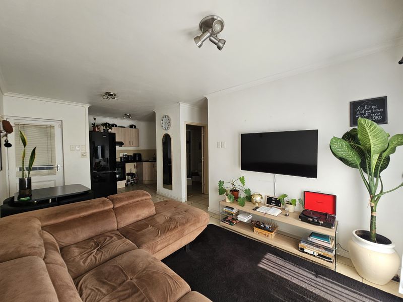 Open-plan living area featuring tiled flooring, ceiling spotlights, and an integrated kitchen space with built-in cabinetry.