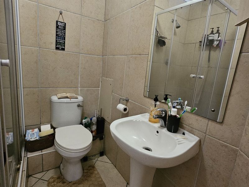 Compact bathroom featuring a pedestal basin, toilet, and shower enclosure with neutral ceramic wall and floor tiling.