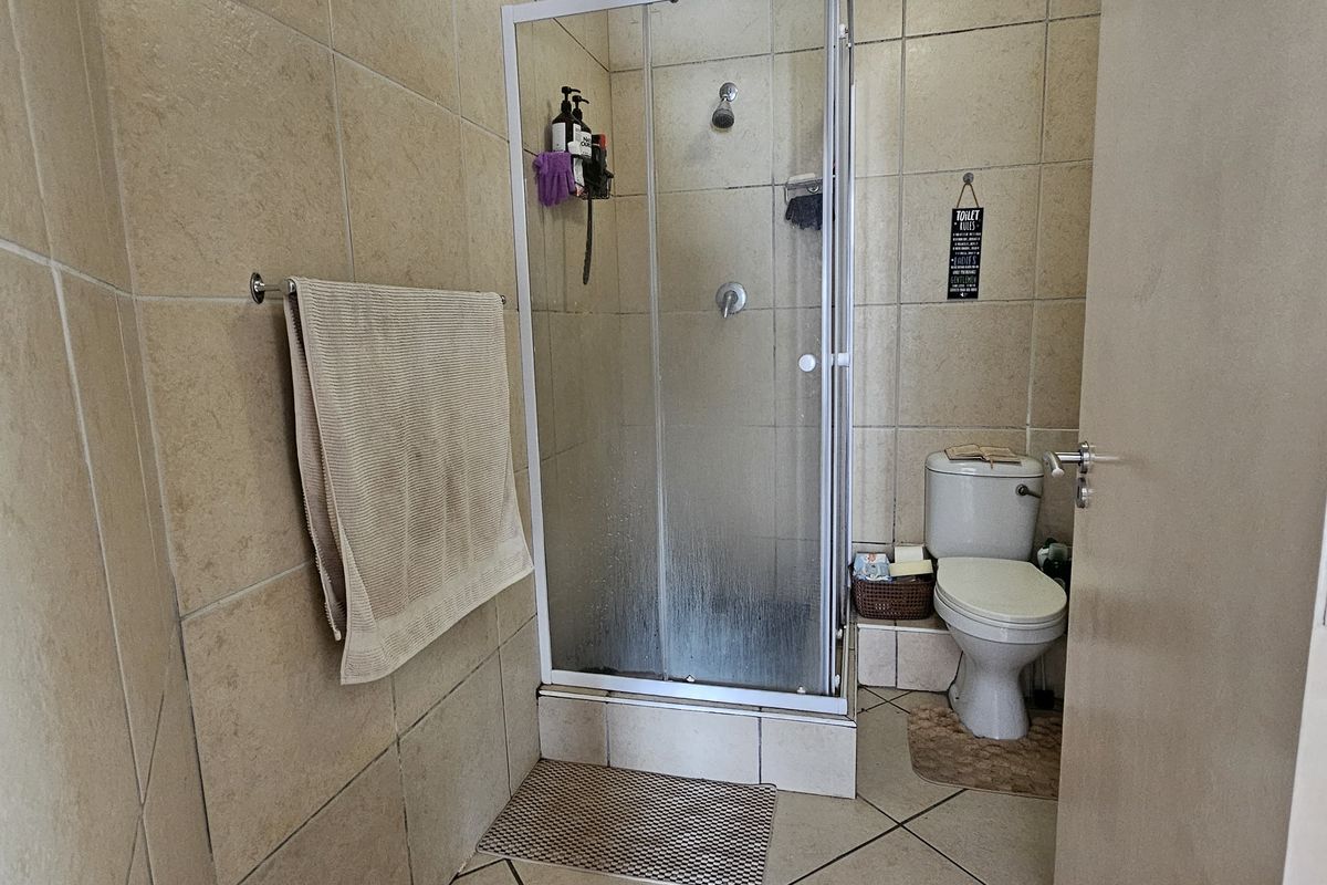 A functional bathroom featuring a glass shower enclosure, toilet, and neutral ceramic tiling throughout.