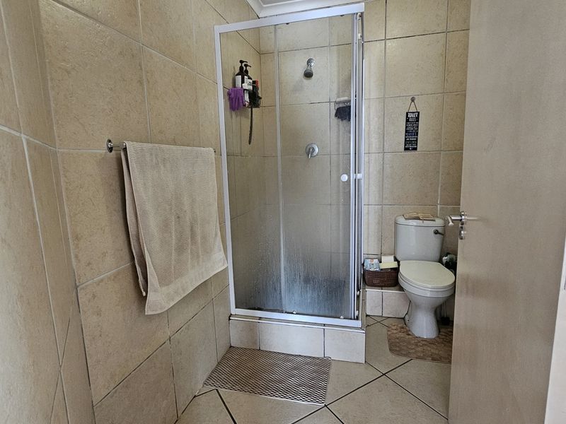 A functional bathroom featuring a glass shower enclosure, toilet, and neutral ceramic tiling throughout.