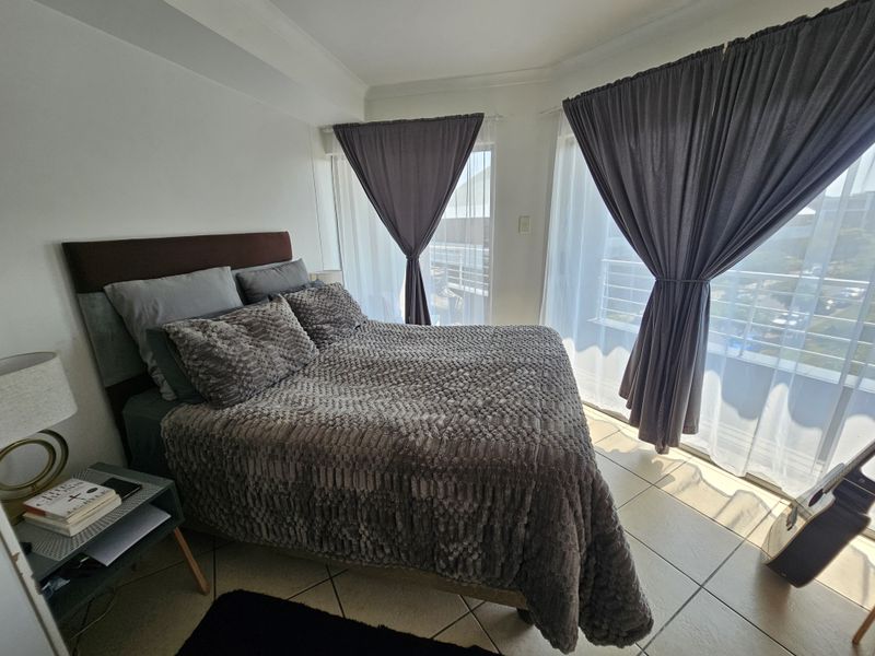 A bright bedroom featuring tiled flooring and large sliding glass doors that provide access to an outdoor balcony area.
