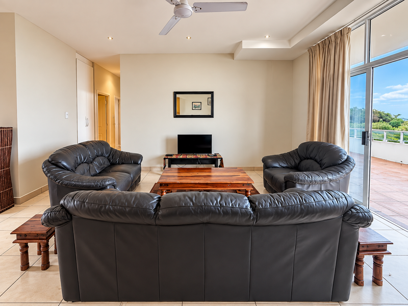 Spacious living room featuring tiled flooring, a ceiling fan, and large sliding glass doors that open onto a balcony with natural light.