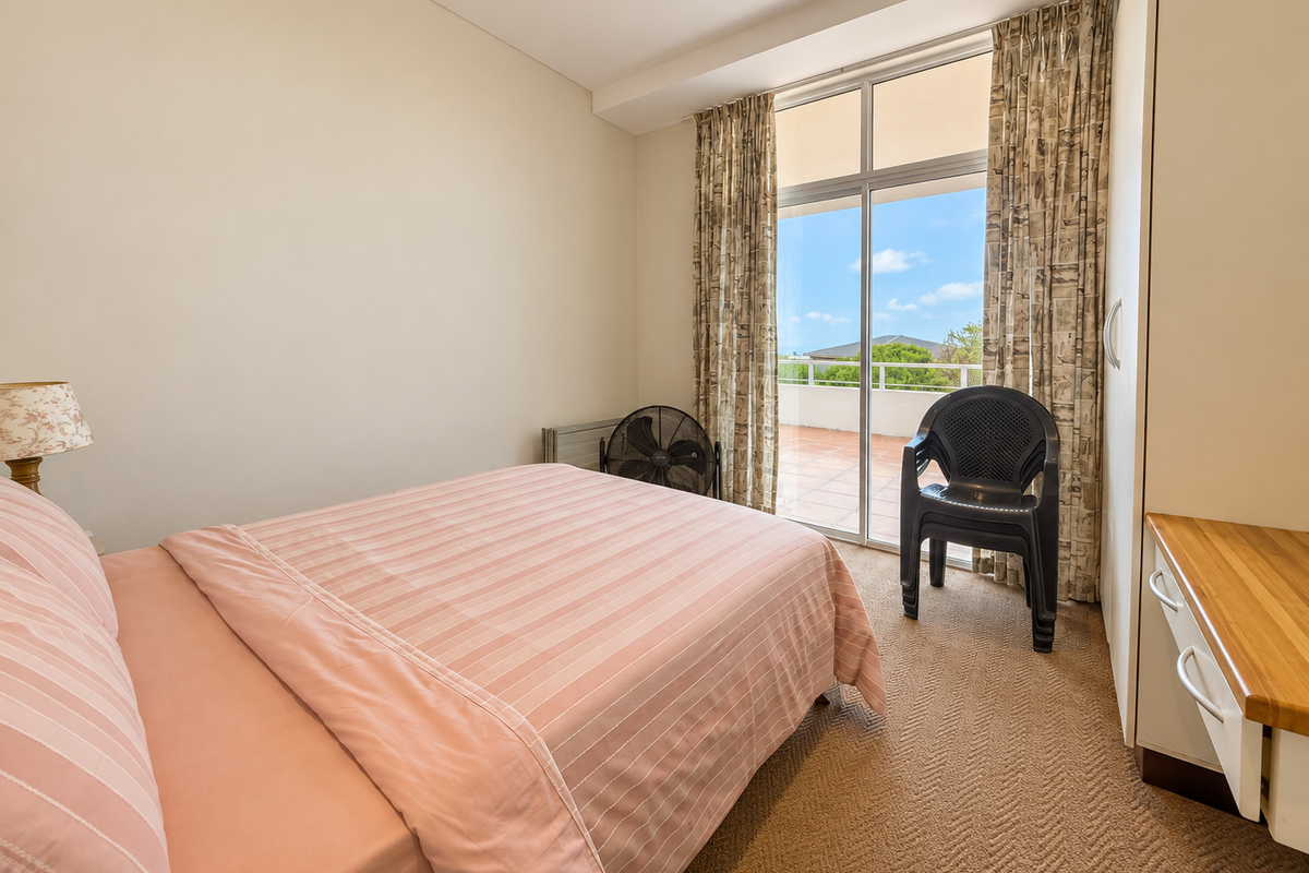 A bedroom featuring built-in wardrobes, a vanity unit, and sliding glass doors that open onto a private balcony with outdoor views.