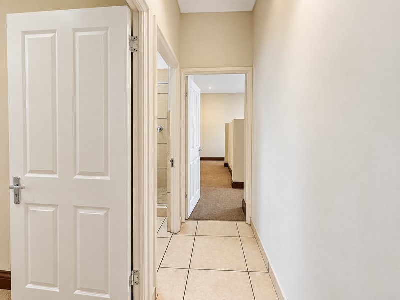 A clean, neutral hallway featuring tiled flooring and access to adjacent rooms, including a bathroom and bedroom area.