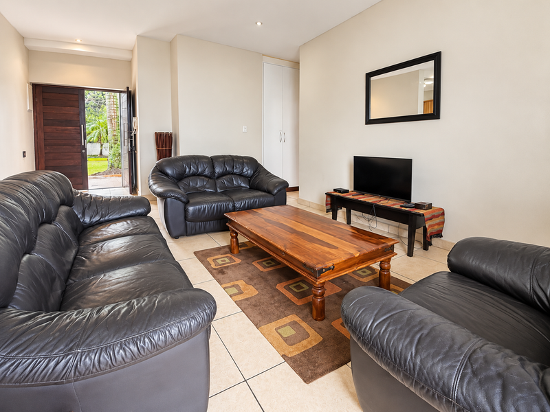 A spacious living room featuring tiled flooring, recessed lighting, and a built-in storage cupboard, with direct access to the exterior garden area.