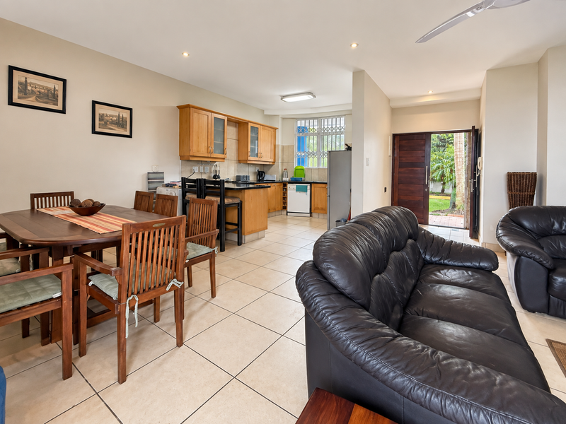 Open-plan living and dining area featuring tiled floors, a functional kitchen with wooden cabinetry, and direct access to the rear garden.
