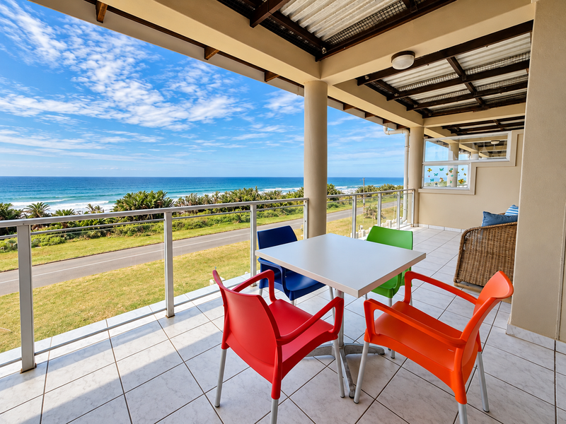 Spacious covered balcony featuring tiled flooring and metal railings, offering expansive ocean and coastal views.